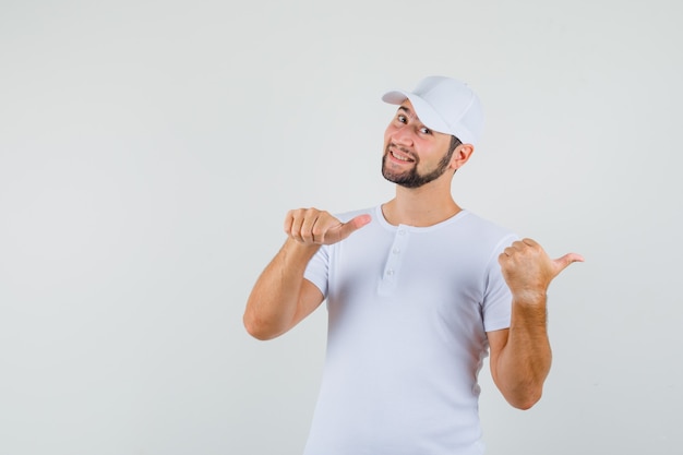 Young man pointing back in t-shirt and looking happy. front view.