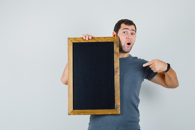 Young man pointing at blackboard in grey t-shirt and looking confident 