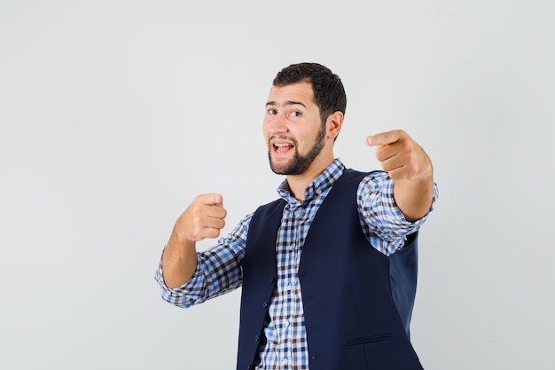 Young man pointing at camera in shirt, vest and looking confident , front view.