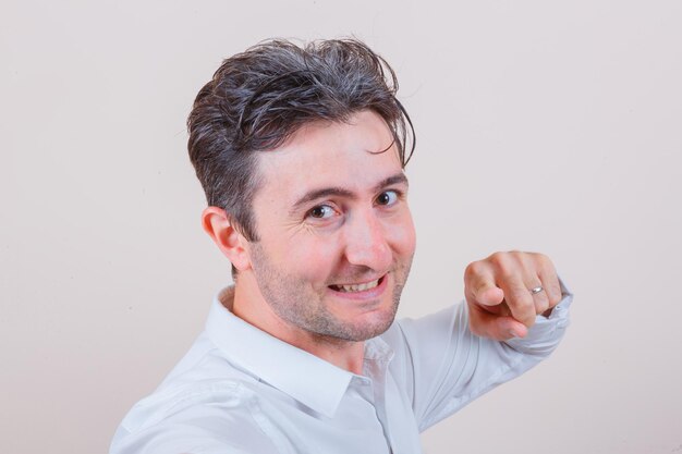 Young man pointing at camera in white shirt and looking cheery