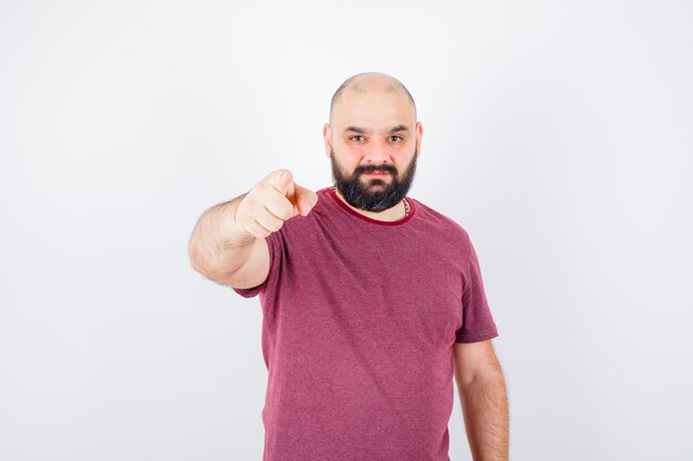 Young man pointing at camera with index finger in pink t-shirt and looking serious , front view.