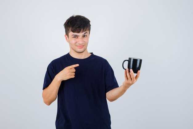 Молодой человек, указывая на чашку в черной футболке и глядя нерешительно, вид спереди.
