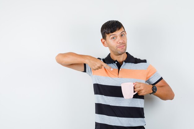 Young man pointing at cup of drink in t-shirt and looking pleased