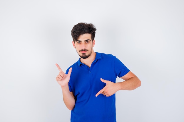 Young man pointing different directions with index fingers in blue t-shirt and looking serious