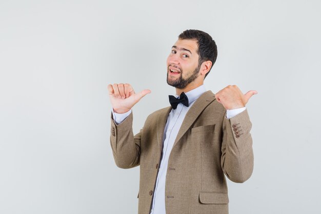 Young man pointing double thumbs up back in suit and looking confident. front view.