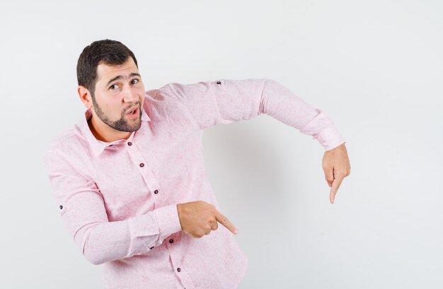 Young man pointing down in pink shirt and looking confident