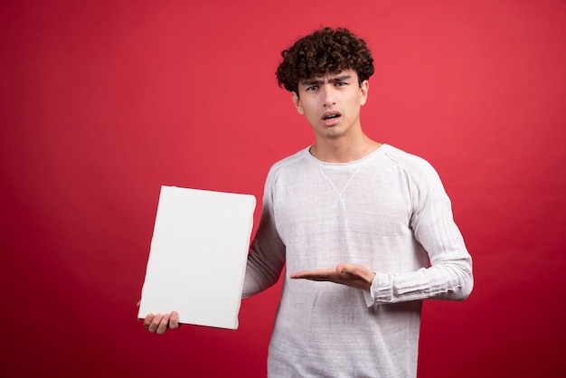 Young man pointing at empty canvas with angry stare.