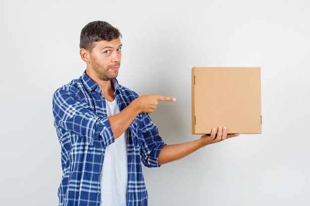 Young man pointing finger at cardboard box in shirt front view.