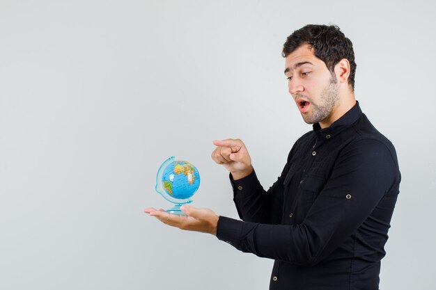 Молодой человек указывая пальцем на земной шар в черной рубашке