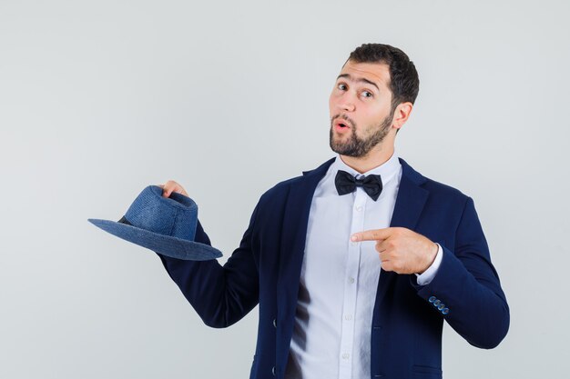 Young man pointing finger at hat in suit and looking pretty. front view.