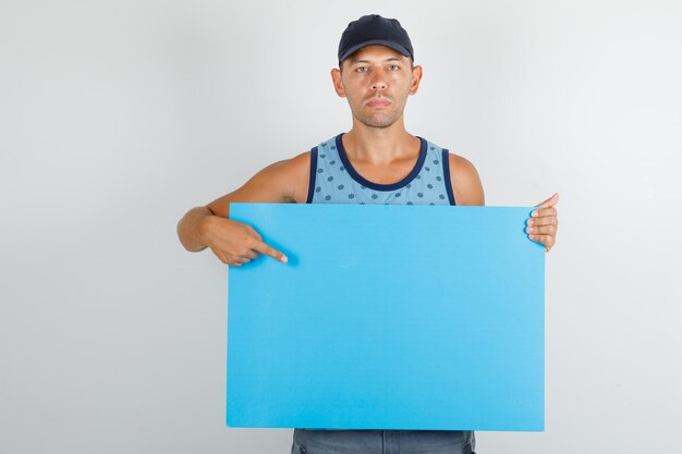 Young man pointing finger at poster in blue singlet with cap