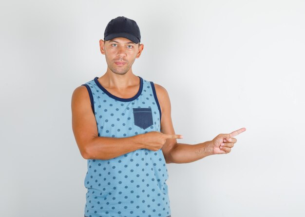 Young man pointing fingers away in blue singlet with cap