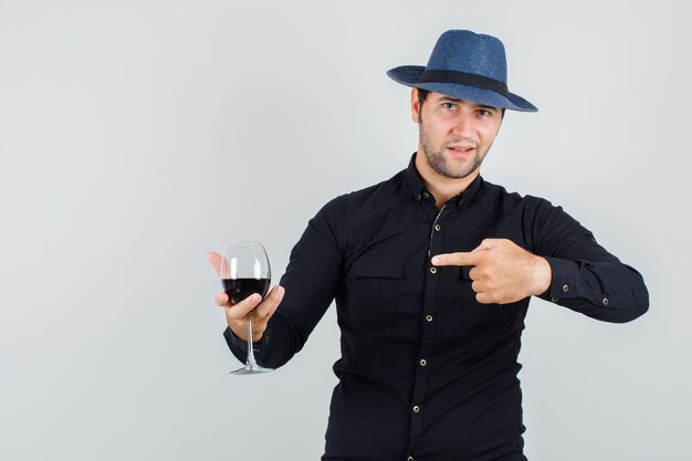 Young man pointing at glass of alcohol in black shirt