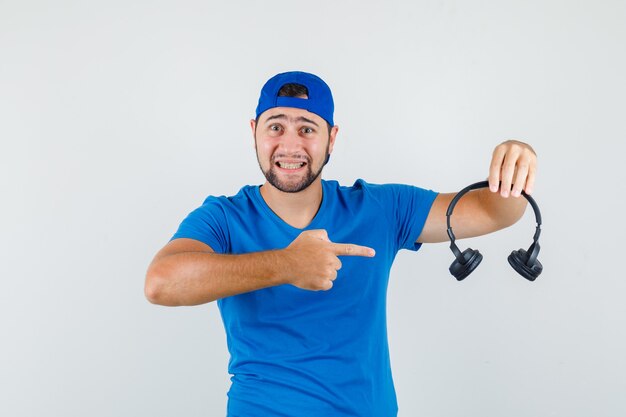 Молодой человек указывает на наушники в синей футболке и кепке и выглядит позитивно