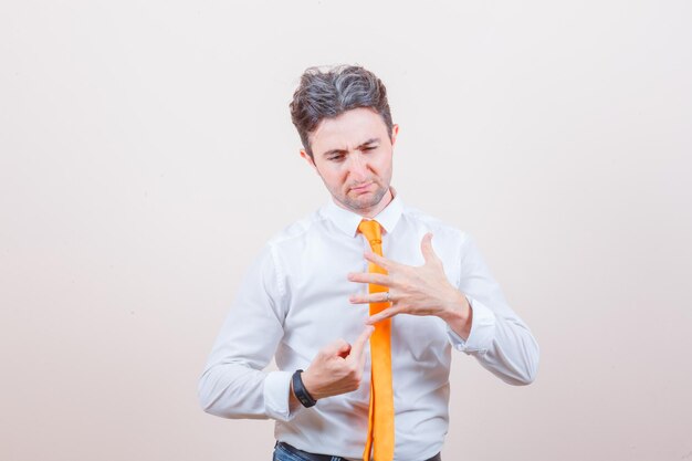 Young man pointing at his five fingers in shirt, jeans and looking sad