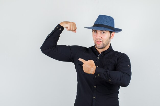 黒のシャツ、帽子で彼の筋肉を指して、強く見える若い男。