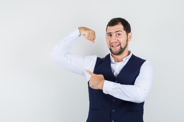 Young man pointing at his muscle in shirt, vest and looking strong