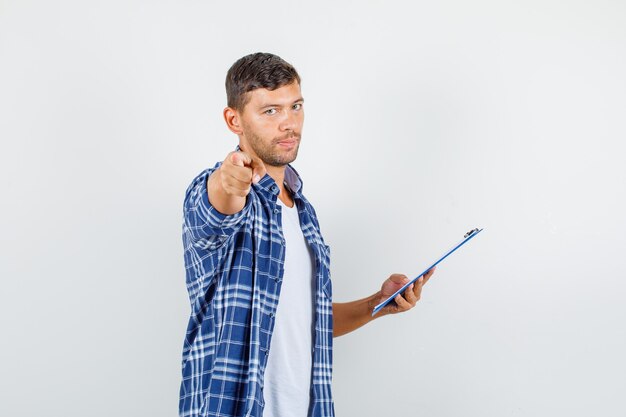 Young man pointing and holding clipboard in shirt and looking ill. front view.