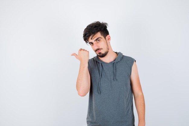 Young man pointing left in gray t-shirt and looking serious