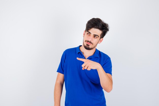 Young man pointing left with index finger in blue t-shirt and looking serious