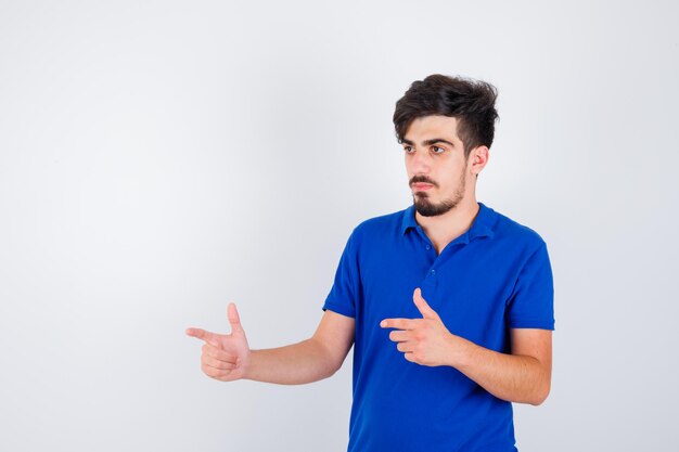 Young man pointing left with index fingers in blue t-shirt and looking serious