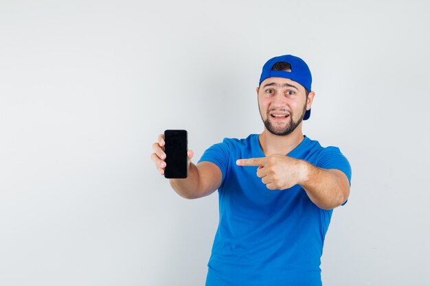 Young man pointing at mobile phone in blue t-shirt and cap and looking pleased