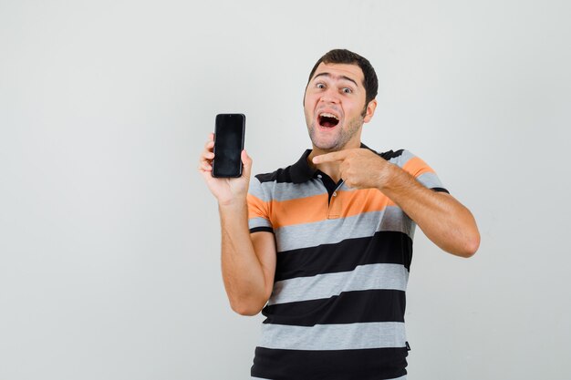 Young man pointing at phone in t-shirt and looking contented