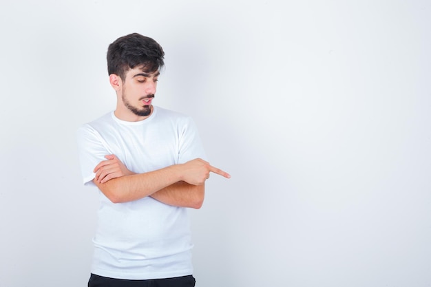 Young man pointing to the right side in t-shirt and looking focused