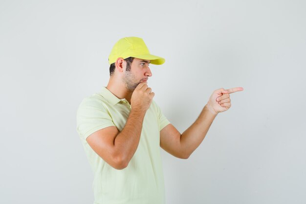 Young man pointing to the right side in yellow uniform and looking hesitant  