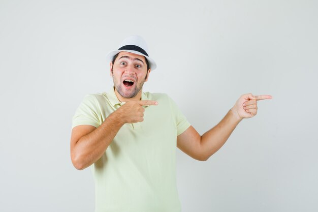 Young man pointing to the side in t-shirt hat and looking amazed 