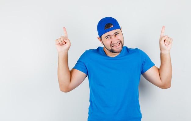 Young man pointing up in blue t-shirt and cap and looking lucky