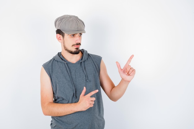 Young man pointing up in gray t-shirt and cap and looking serious