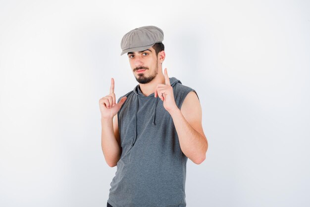 Young man pointing up in gray t-shirt and cap and looking serious