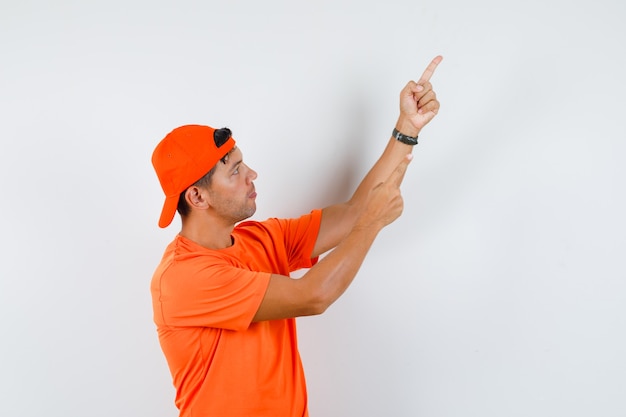 Young man pointing up in orange t-shirt and cap and looking focused