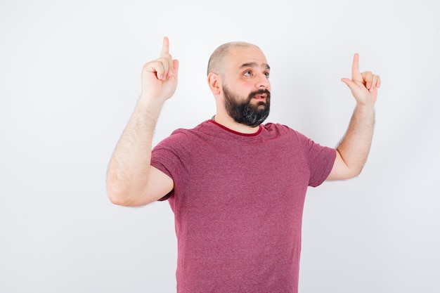 Young man pointing up in pink t-shirt and looking optimistic. front view.