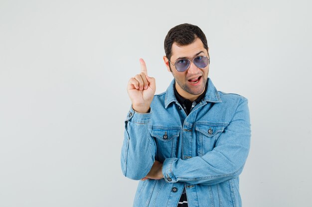 Young man pointing up in t-shirt, jacket and looking confident. front view.