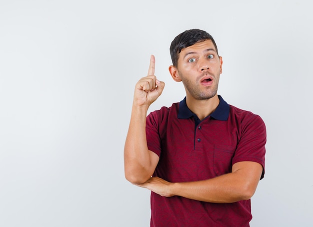 Young man pointing up in t-shirt and looking excited. front view.