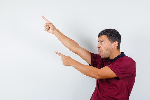 Young man pointing up in t-shirt and looking focused , front view.