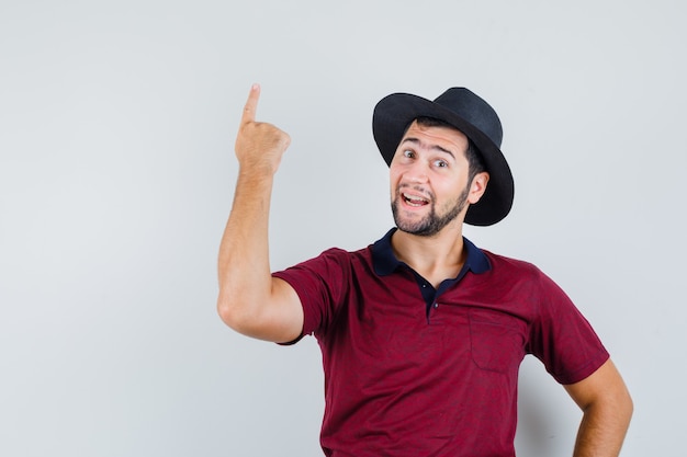 Foto gratuita giovane uomo rivolto verso l'alto mentre parla in maglietta rossa, cappello e guardando concentrato, vista frontale.