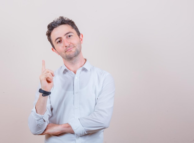 Young man pointing up in white shirt and looking optimistic