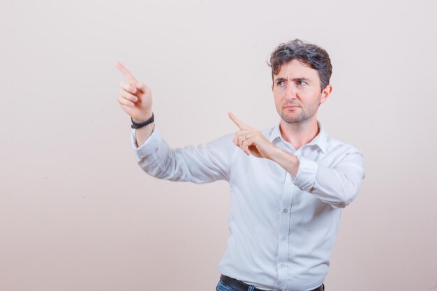 Young man pointing at upper left corner in white shirt, jeans and looking focused