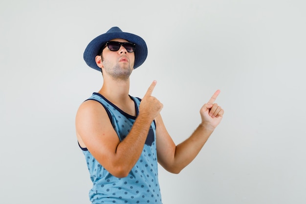 Young man pointing at upper right corner in blue singlet, hat and looking focused. front view.