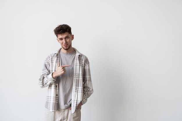 Young man points finger to side on white background