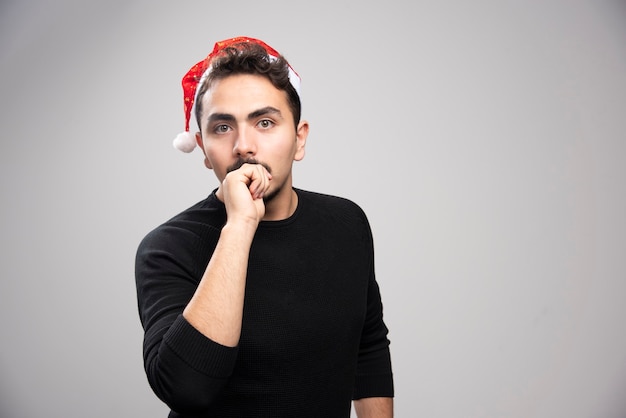 Young man posing in Santa's red hat over a gray wall. 