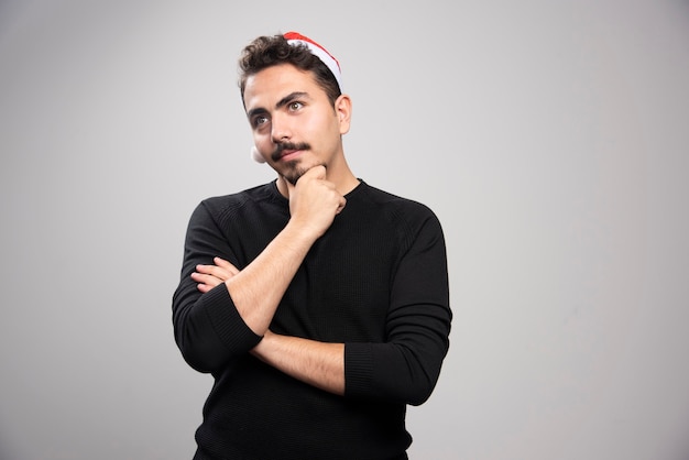 Young man posing in Santa's red hat thinking .