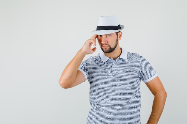 Young man posing in striped t-shirt,hat and looking macho , front view.