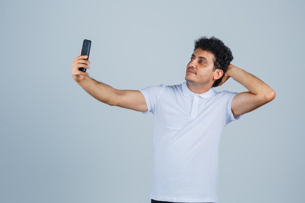 Young man posing while taking selfie in white t-shirt and looking cute. front view.