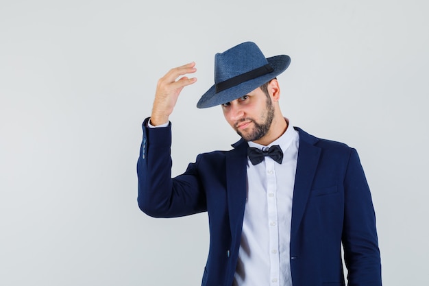 Free photo young man posing with hand to his hat in suit and looking pretty , front view.