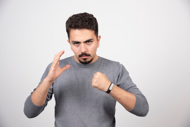 A young man posing with hands over a white wall.