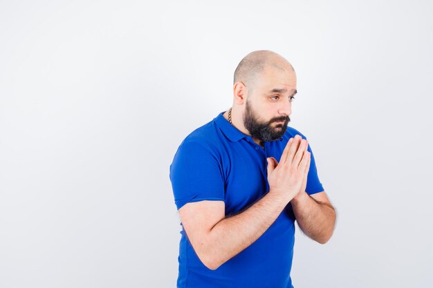 파란색 셔츠 전면 보기에서 뭔가를 위해 기도하는 젊은 남자.